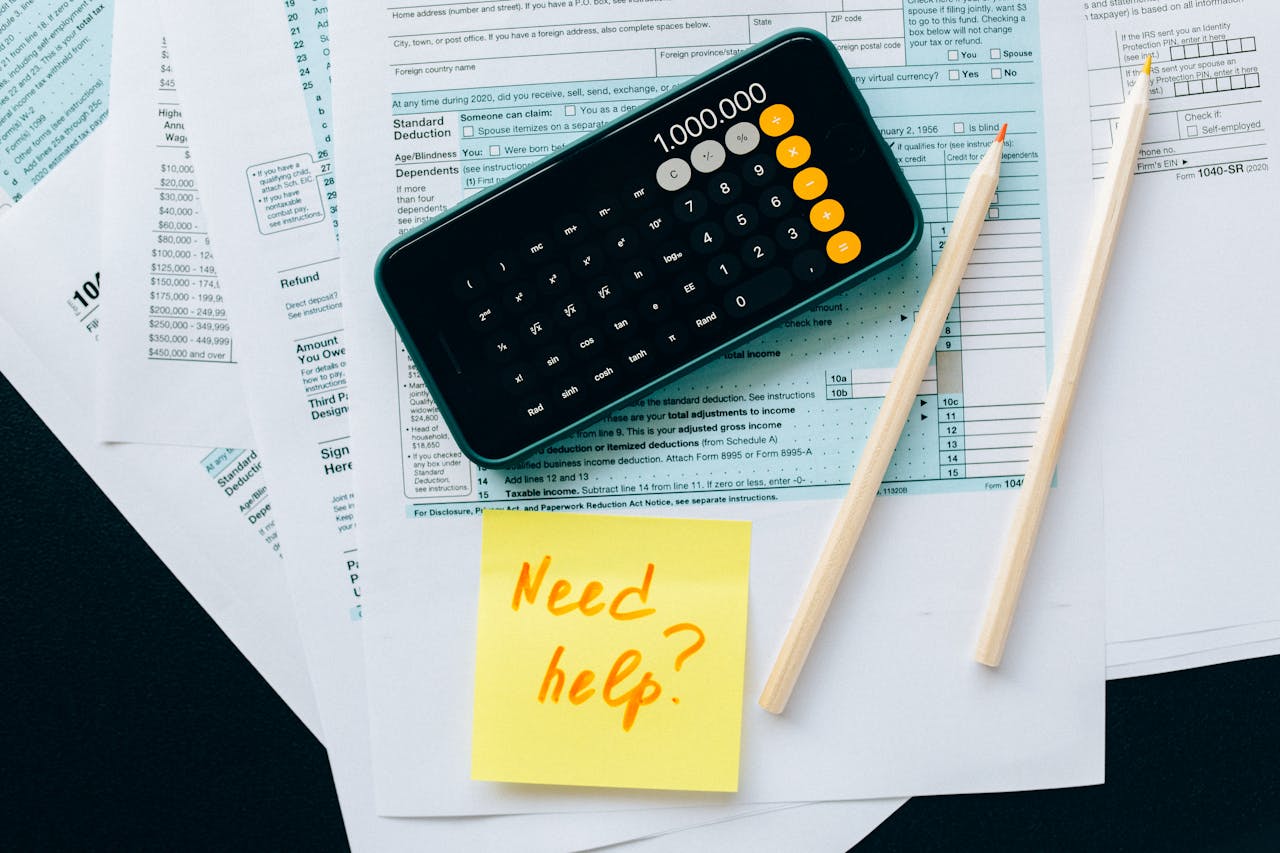 Top view of financial papers with a calculator, pencils, and a note saying Need help? indicating tax or accounting assistance.